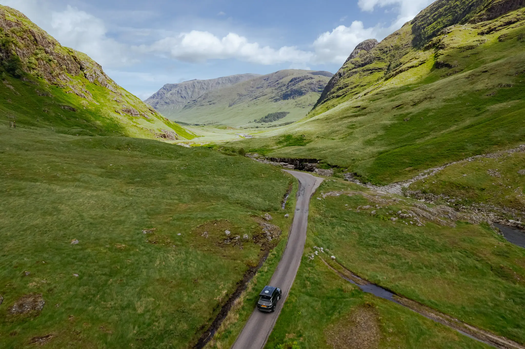 drone shot of a campervan driving through a green valley in Scotland