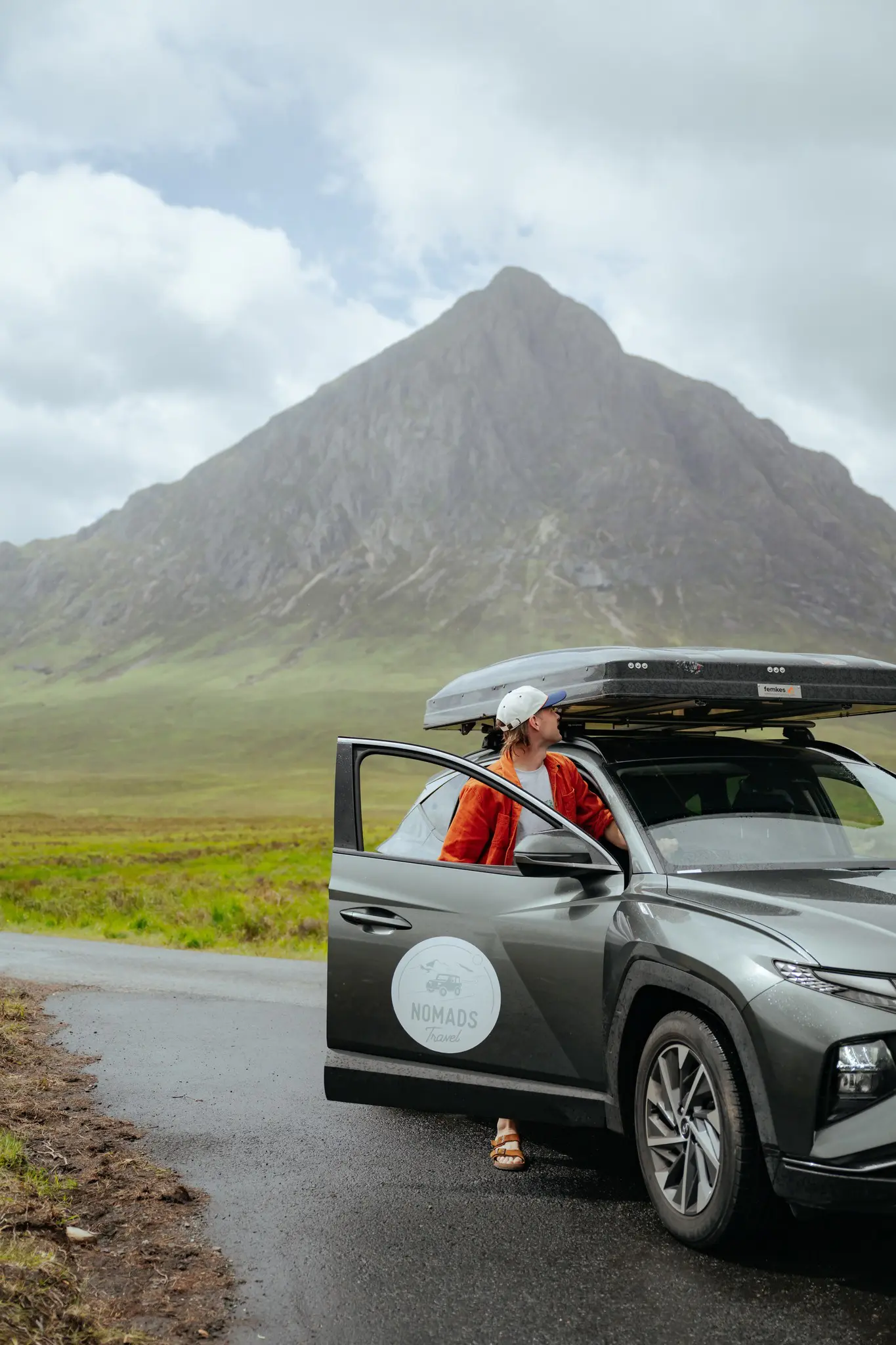 person in car with rooftop tent looking at mountain in Scotland