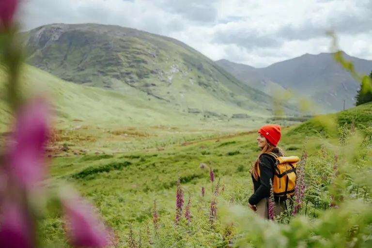 Frau beim Wandern in den schottischen Highlands mit roter Mütze und gelbem Rucksack
