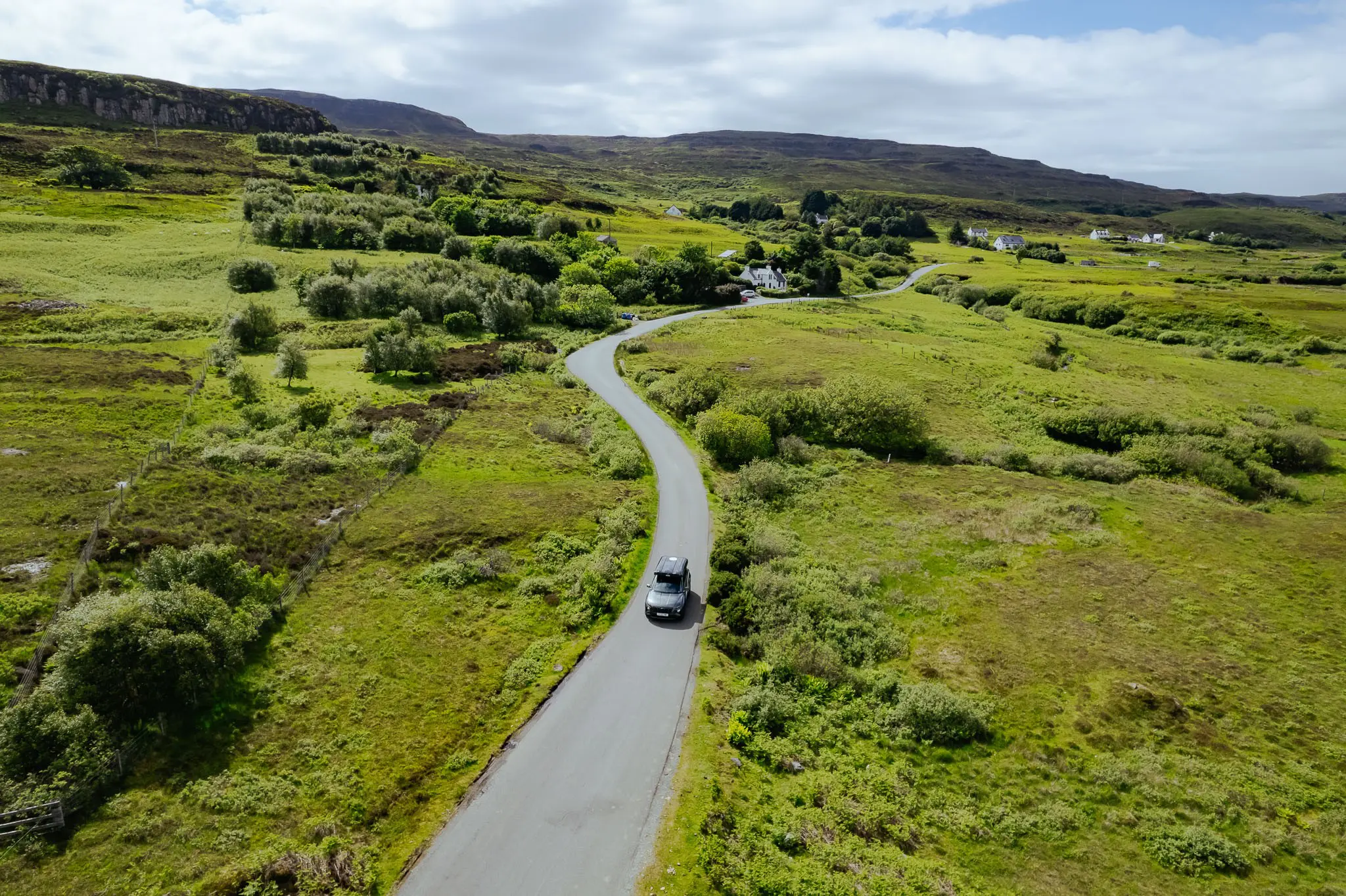 drone shot of a car driving on a winding road in Scotland