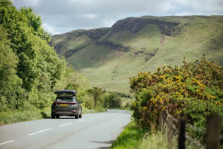 Auto mit Dachbox auf einer malerischen Straße in Schottland