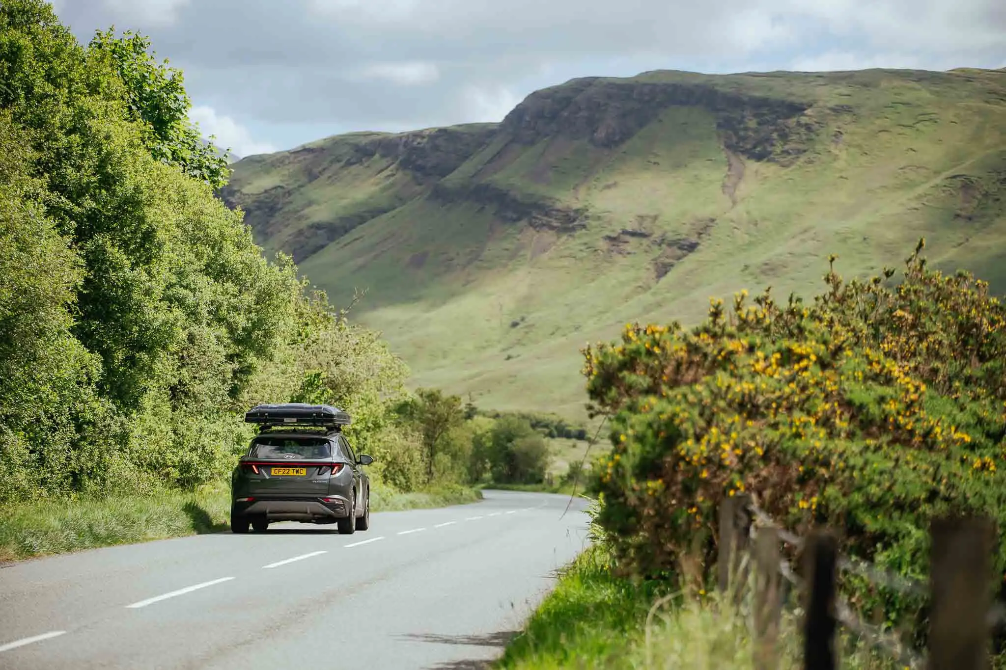 car with roof box driving on a scenic road in Scotland