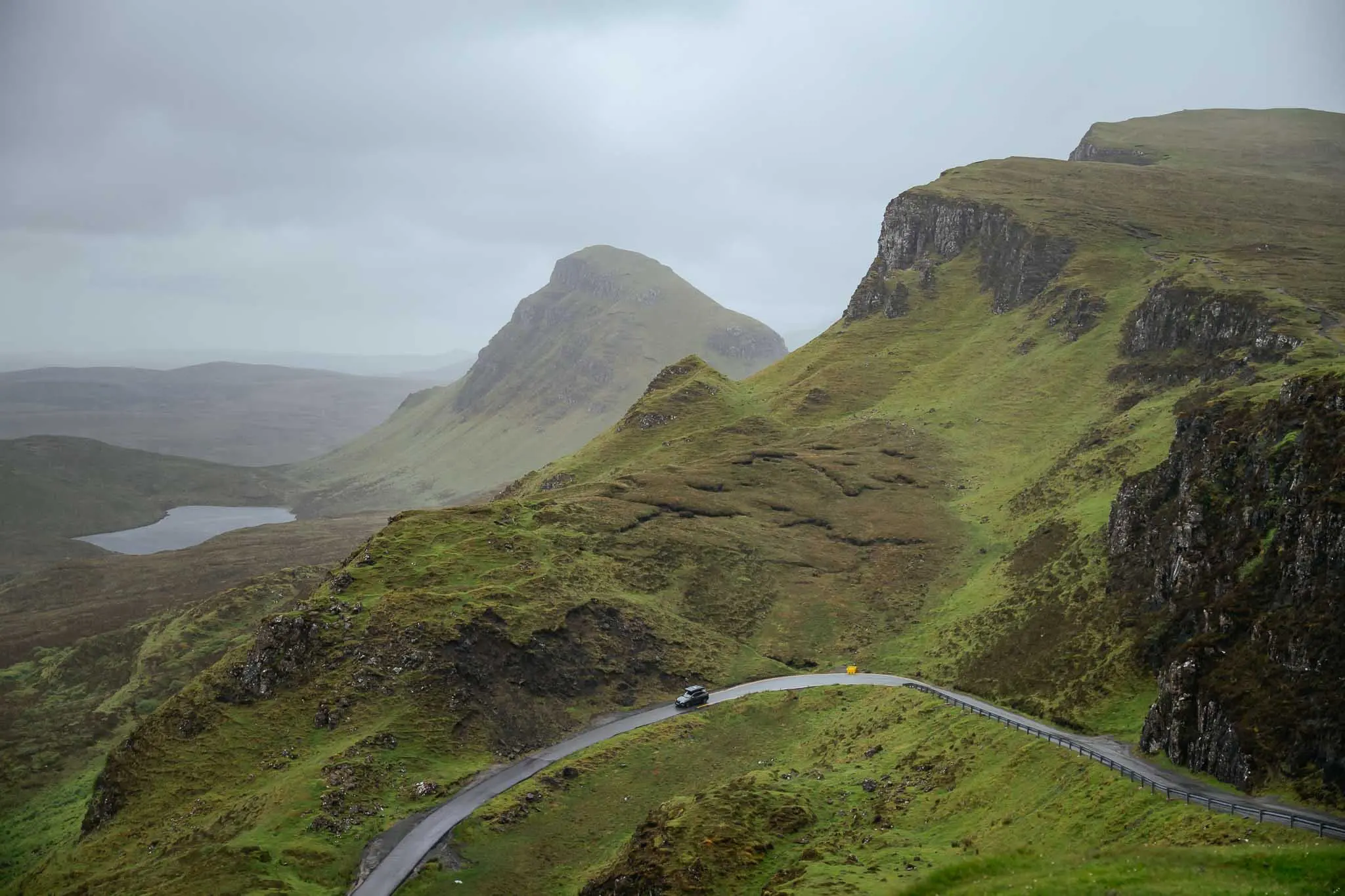 car driving on winding road through green Scottish mountains
