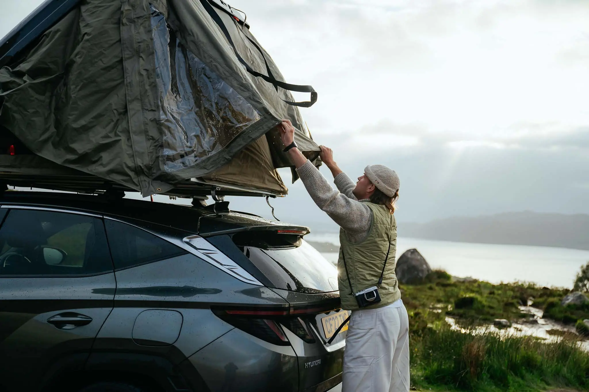 person setting up rooftop tent on car in Scottish landscape