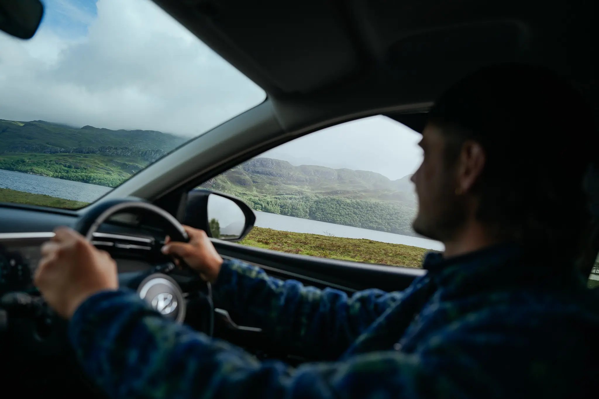 man driving car through Scottish Highlands with loch and mountains