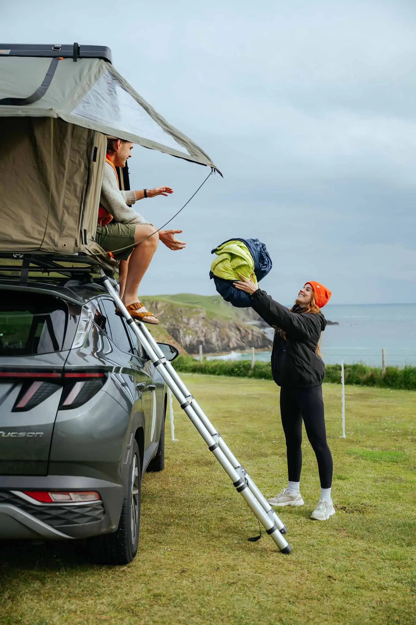 couple setting up rooftop tent on car by the coast in Scotland