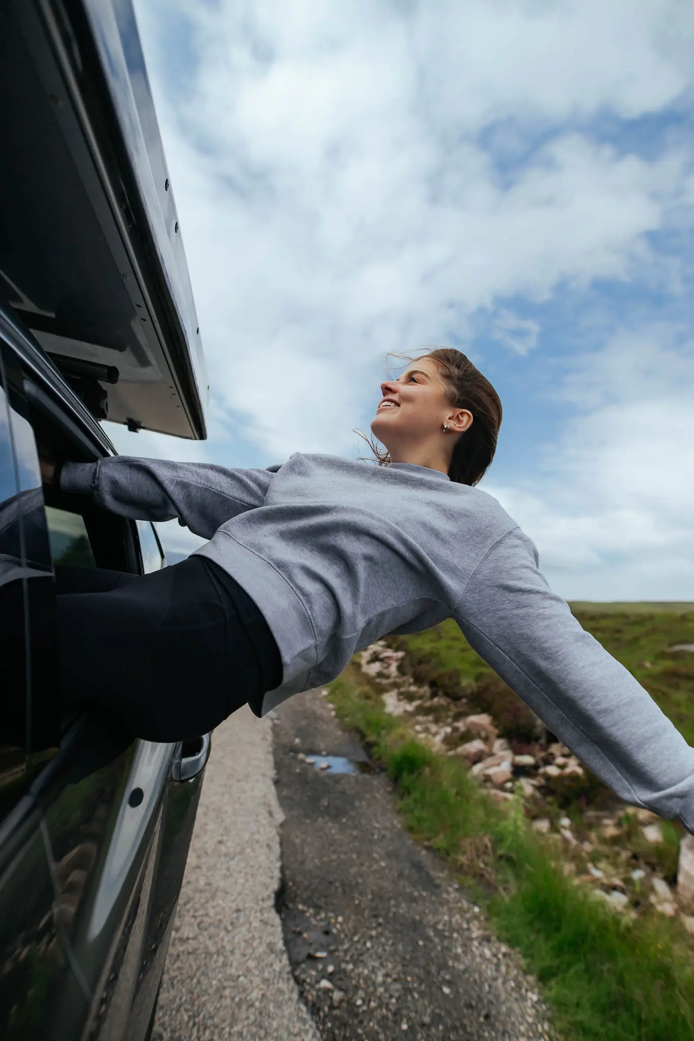 young woman leaning out of car window on a scenic road in Scotland