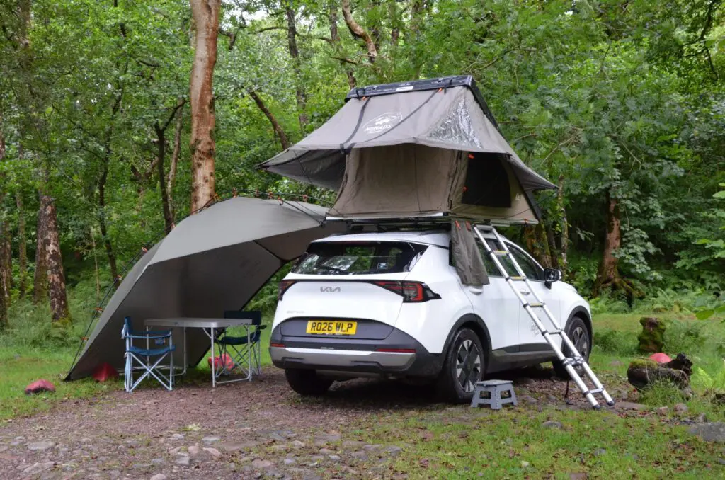 white car with rooftop tent and awning set up in a forest