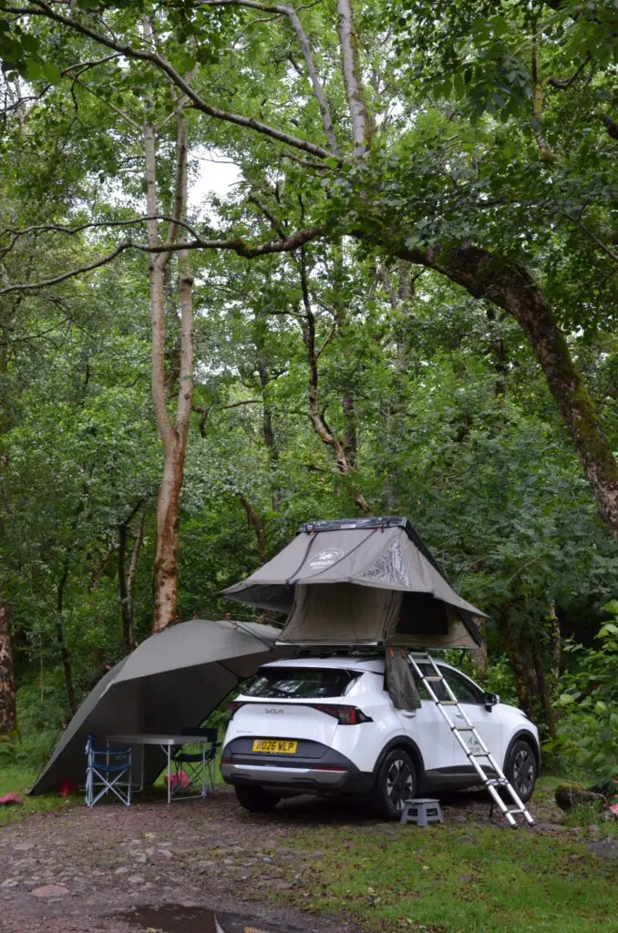 weißer SUV mit Dachzelt und Markise auf einem Waldcampingplatz