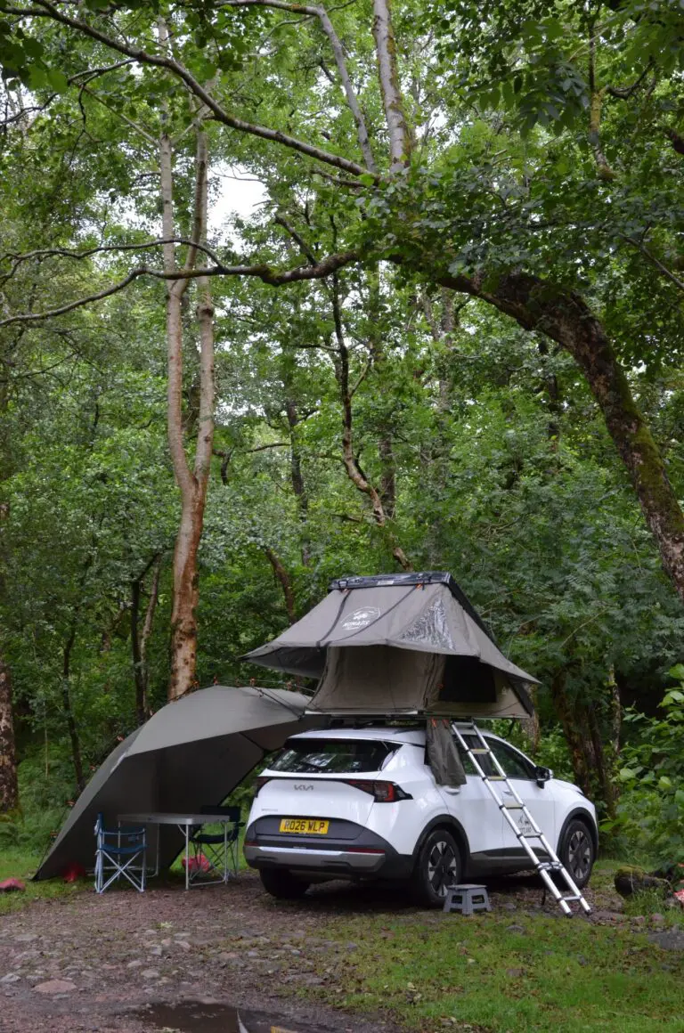 weißer SUV mit Dachzelt und Markise auf einem Waldcampingplatz
