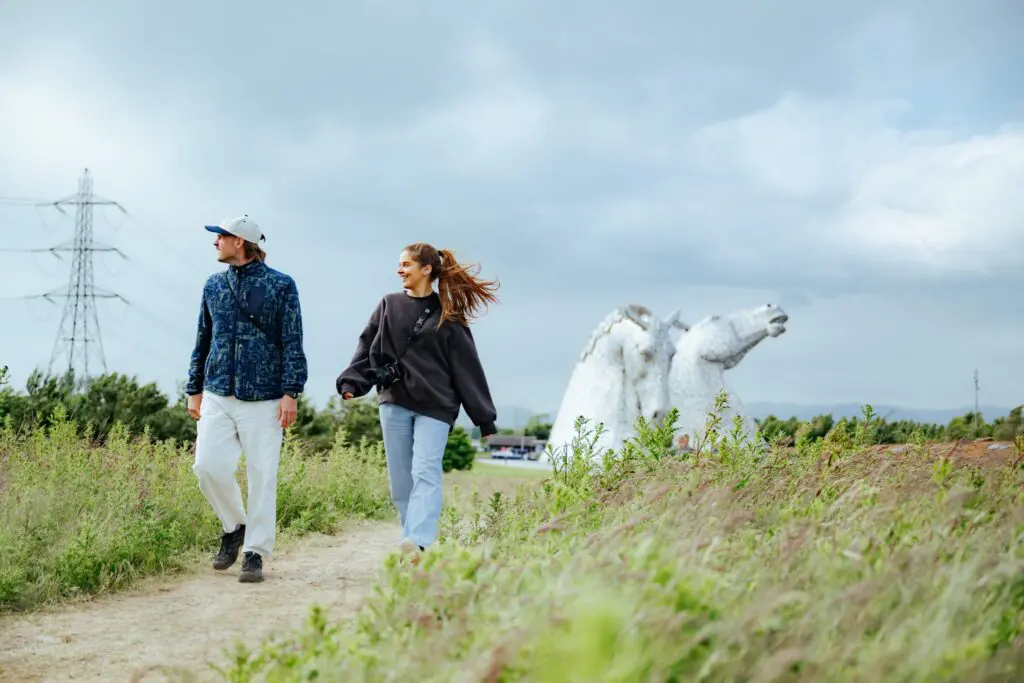 couple walking past The Kelpies in Scotland