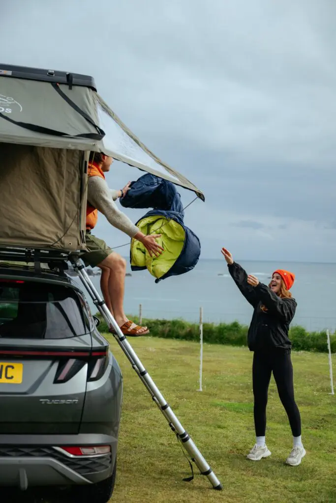 couple packing sleeping bags from rooftop tent in Scotland