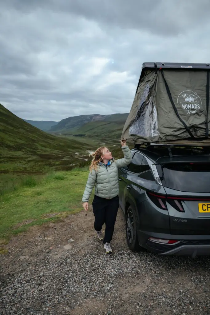 woman opening rooftop tent on car in Scottish Highlands