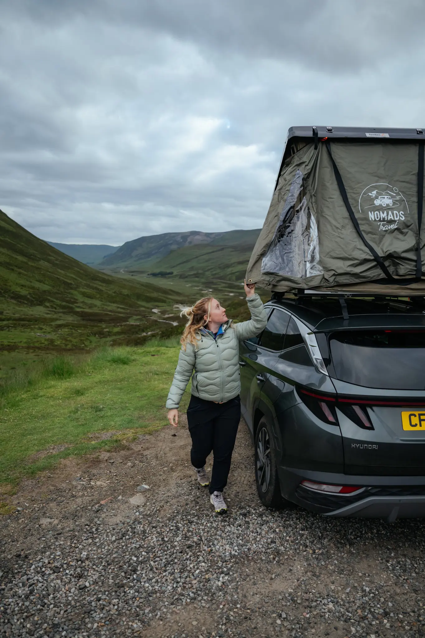 woman opening rooftop tent on car in Scottish Highlands