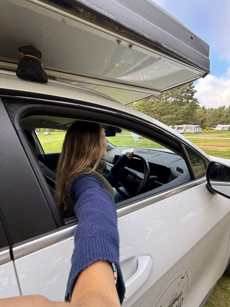 woman driving a car with a rooftop tent at a campsite