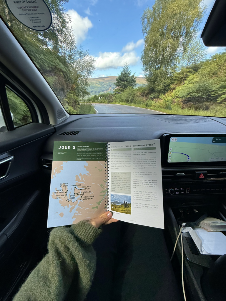 person holding a travel guide inside a car in Scotland