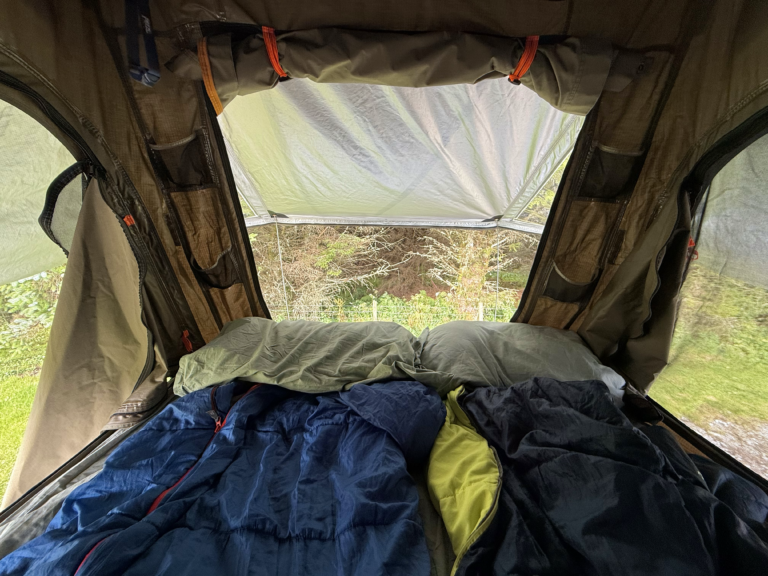 inside a rooftop tent with sleeping bags looking out at forest