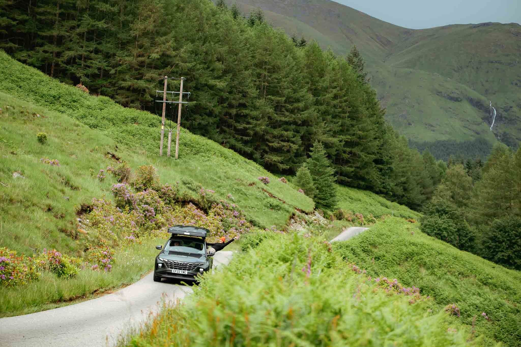 car with roof tent driving on a winding road in the Scottish Highlands
